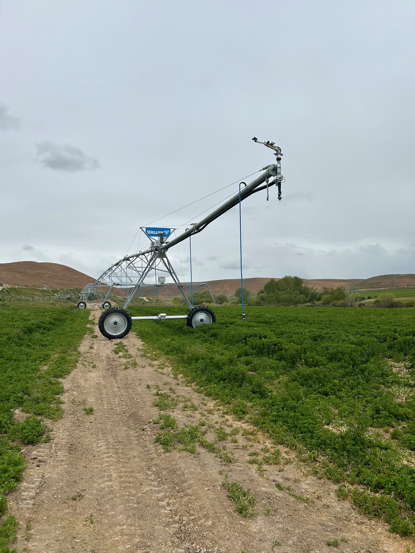 A center-pivot irrigation system watering a green alfalfa field below the Gem County hills