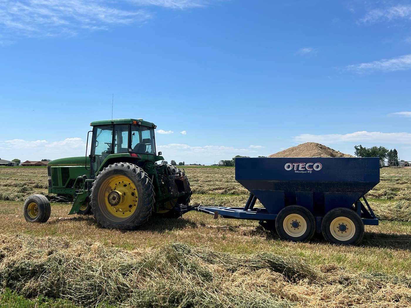 A John Deere tractor towing the district's loaded blue OTECO pivot track filler across a field